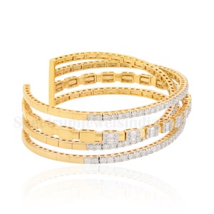 May include: A gold-toned cuff bracelet with four parallel bands. The bracelet features a combination of smooth gold sections and sections encrusted with small, sparkling diamonds. The design is open-ended, allowing for easy wear.