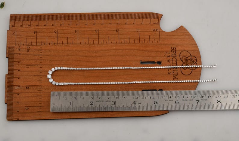 May include: A delicate silver necklace with clear, round gemstones, displayed on a wooden ruler. The necklace is approximately 18 inches long. The ruler shows measurements in inches, and the necklace is laid out for display.