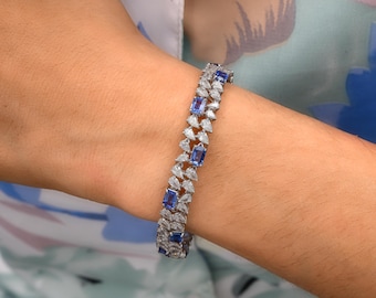 May include: A silver-toned bracelet featuring a double row of pear-shaped clear stones and rectangular blue stones. The design consists of alternating clusters of white pear-cut stones and single rectangular blue stones set in a metallic band.