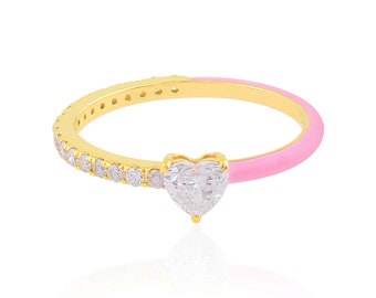 May include: A gold-colored ring with a heart-shaped clear stone and a pink enamel band. The ring features a row of small, clear stones along one side. The heart-shaped stone is the focal point of the ring.