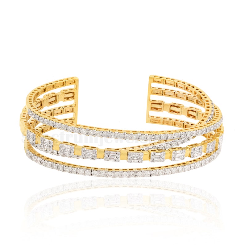 May include: A gold-toned cuff bracelet with three rows of sparkling white gemstones. The bracelet has an open design, with the gemstones set in a channel style. The bracelet is a luxurious piece of jewelry.