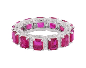 Könnte beinhalten: Ein silberner Eternity-Ring mit rechteckigen, leuchtend rosa Edelsteinen. Zwischen jedem rosa Stein befinden sich kleine, klare Akzentsteine, die ein durchgehendes Band aus Farbe und Glanz bilden. Der Ring ist vor weißem Hintergrund platziert.