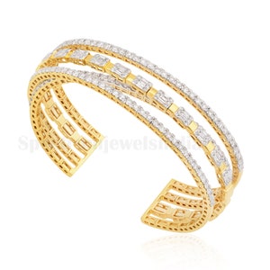 May include: A gold-toned cuff bracelet with three parallel bands. Each band is encrusted with small, sparkling diamonds. The center band features rectangular diamond accents. The bracelet has an open design.
