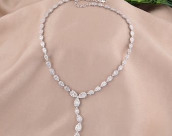 May include: A dazzling silver necklace featuring a series of pear-shaped and baguette-cut gemstones. The necklace has a delicate chain and a pendant of cascading gemstones. The jewelry is displayed on a neutral-toned fabric.