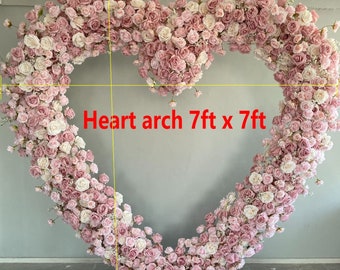 Puede incluir: Un arco floral en forma de corazón hecho de rosas rosas y blancas, que mide 7 pies por 7 pies. El arco está decorado con pequeñas flores blancas y se encuentra sobre una fila de rosas rosas y blancas, que mide 60 pulgadas por 16 pulgadas.