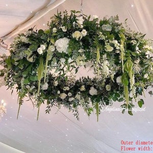 May include: A large, circular floral arrangement hanging from the ceiling. The arrangement is made up of white flowers and greenery, with a diameter of 4 feet and a flower width of 1.2 feet.
