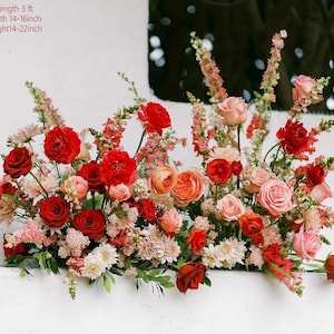 May include: A vibrant floral arrangement featuring a variety of blooms in shades of red, pink, and peach. The arrangement is approximately 3 feet long, 14-16 inches wide, and 14-22 inches high. Roses, carnations, and other flowers create a lush display.
