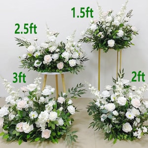 May include: Arrangement of white roses and greenery, some on gold stands and others on a small table. The arrangements are labeled with heights: 1.5ft, 2ft, 2.5ft, and 3ft. Ideal for weddings or events.