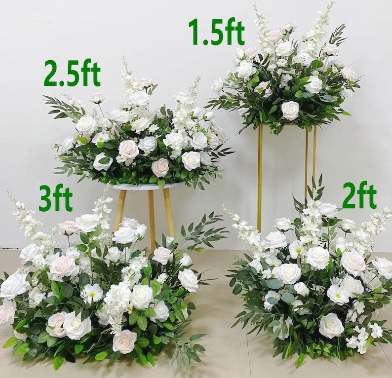 May include: Arrangement of white roses and greenery, some on gold stands and others on a small table. The arrangements are labeled with heights: 1.5ft, 2ft, 2.5ft, and 3ft. Ideal for weddings or events.