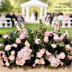 May include: A floral arrangement featuring pink and black roses, hydrangeas, and greenery. The arrangement is approximately 2 feet long, 14-16 inches wide, and 16-24 inches high. The flowers are arranged in a low, rectangular shape, suitable for a wedding or event.