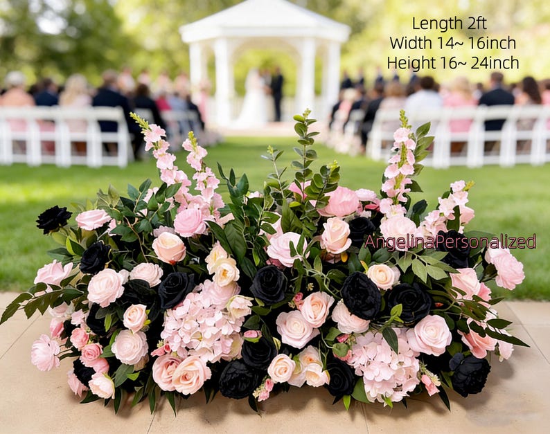 May include: A floral arrangement featuring pink and black roses, hydrangeas, and greenery. The arrangement is approximately 2 feet long, 14-16 inches wide, and 16-24 inches high. The flowers are arranged in a low, rectangular shape, suitable for a wedding or event.