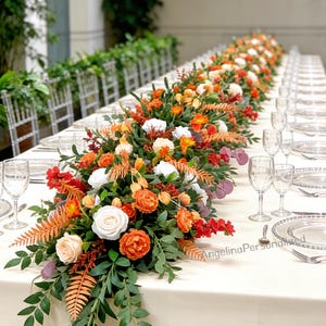 May include: A long table set for a formal event, adorned with a vibrant floral centerpiece. The arrangement features orange, white, and red flowers with green foliage. Clear glassware and place settings are arranged on a cream-colored tablecloth.