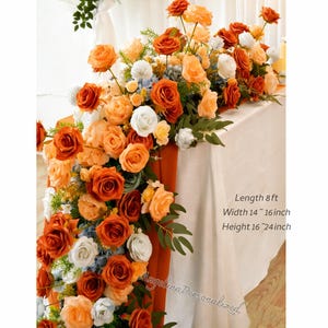 May include: A floral table runner featuring orange, peach, and white roses, with accents of blue and green foliage. The runner is approximately 8 feet long, 14 to 16 inches wide, and 16 to 24 inches high. The text "Angelina Personalized" is visible.