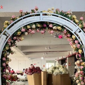 May include: White metal archway decorated with pink, white, and yellow artificial flowers. The archway is in a warehouse setting.