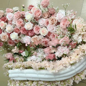 Puede incluir: Un arco de espuma blanca decorado con flores artificiales rosas y blancas. El arco est&aacute; cubierto de una variedad de flores, incluyendo rosas, hortensias y aliento de beb&eacute;.