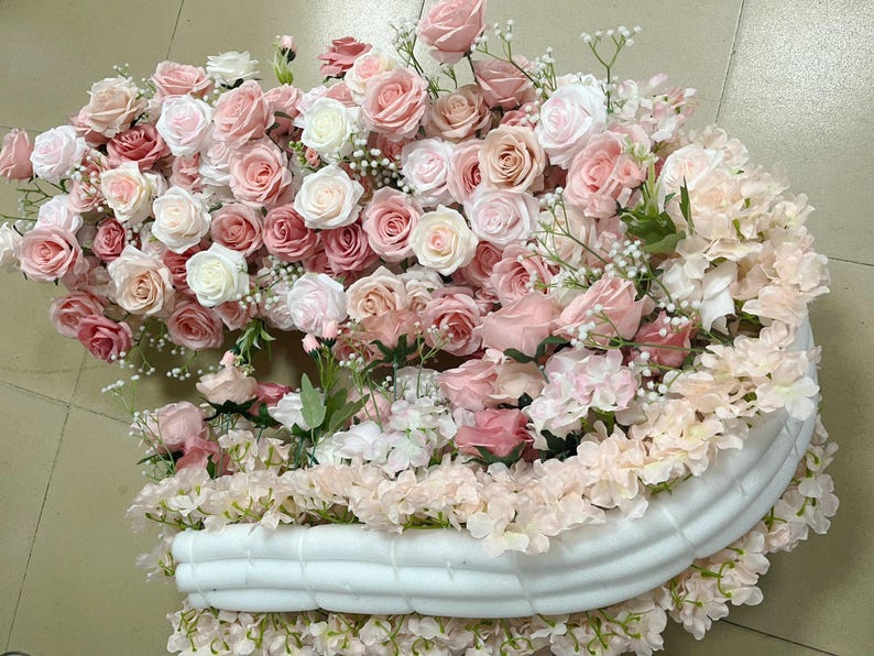 Puede incluir: Un arco de espuma blanca decorado con flores artificiales rosas y blancas. El arco est&aacute; cubierto de una variedad de flores, incluyendo rosas, hortensias y aliento de beb&eacute;.