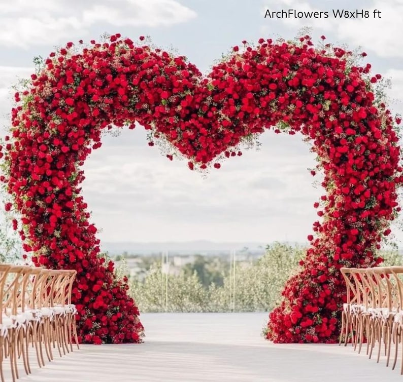 May include: A large heart-shaped floral arch made of red roses, approximately 8 feet wide and 8 feet high, with the text "ArchFlowers W8xH8 ft". The arch is set up for a wedding ceremony, with rows of wooden chairs.