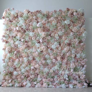May include: A large floral wall backdrop made of artificial flowers in shades of white, blush pink, and dusty rose. The wall is densely packed with roses, hydrangeas, and baby's breath.