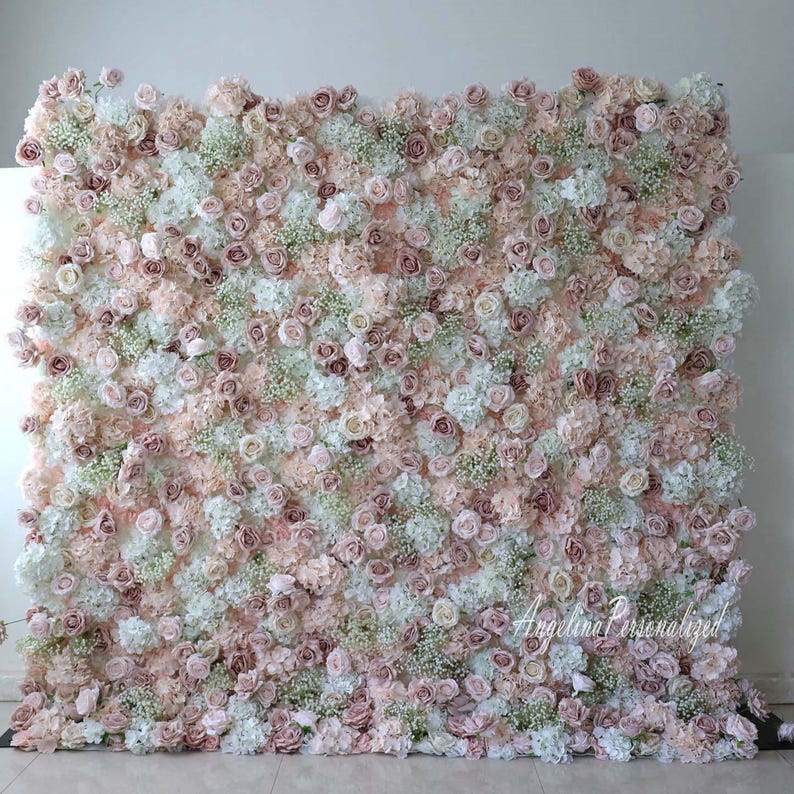 May include: A large floral wall backdrop made of artificial flowers in shades of white, blush pink, and dusty rose. The wall is densely packed with roses, hydrangeas, and baby's breath.