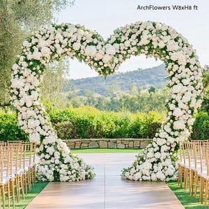 May include: A heart-shaped floral arch, approximately 8 feet wide and 8 feet high, made of white and pink flowers. The arch is set up outdoors with rows of gold chairs on either side, creating a romantic wedding ceremony setting.