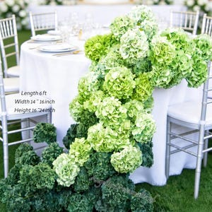 May include: A table decorated with cascading green and light green hydrangea flowers. The table is covered with a white tablecloth and surrounded by silver chairs. The text on the image reads: Length 6 ft, Width 14-16 inch, Height 16-24 inch.