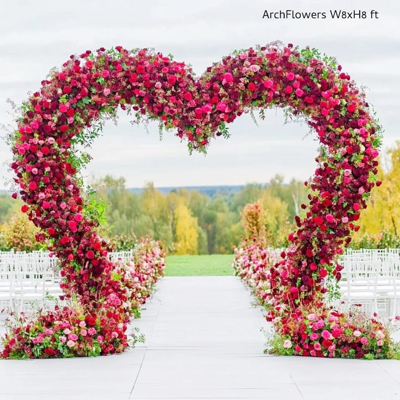 May include: A heart-shaped floral arch, approximately 8 feet wide and 8 feet high, made of red and pink flowers and greenery. The archway is set up outdoors for a wedding or event. The text "ArchFlowers W8xH8 ft" is visible.