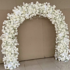 May include: A white floral archway made of white roses, orchids, and baby's breath. The archway is perfect for a wedding ceremony or other special event.