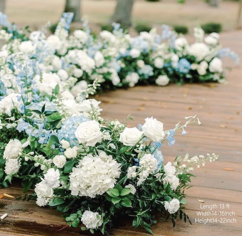 May include: A floral arrangement of white roses, hydrangeas, and blue delphiniums, with green foliage, displayed on a wooden surface. The image text reads: Length 13 ft, Width 35-41 cm, Height 35-56 cm.