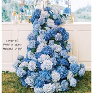 May include: A display of blue and white hydrangeas, with the text "Length 6 ft, Width 14-16 inch, Height 16-24 inch". The flowers are arranged in a cascading design, creating a lush and vibrant floral arrangement. The flowers are on a white surface.