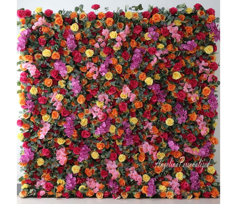 May include: A floral wall backdrop with a variety of artificial flowers in shades of pink, orange, yellow, and red. The flowers are arranged in a dense, lush pattern, creating a vibrant and colorful display.
