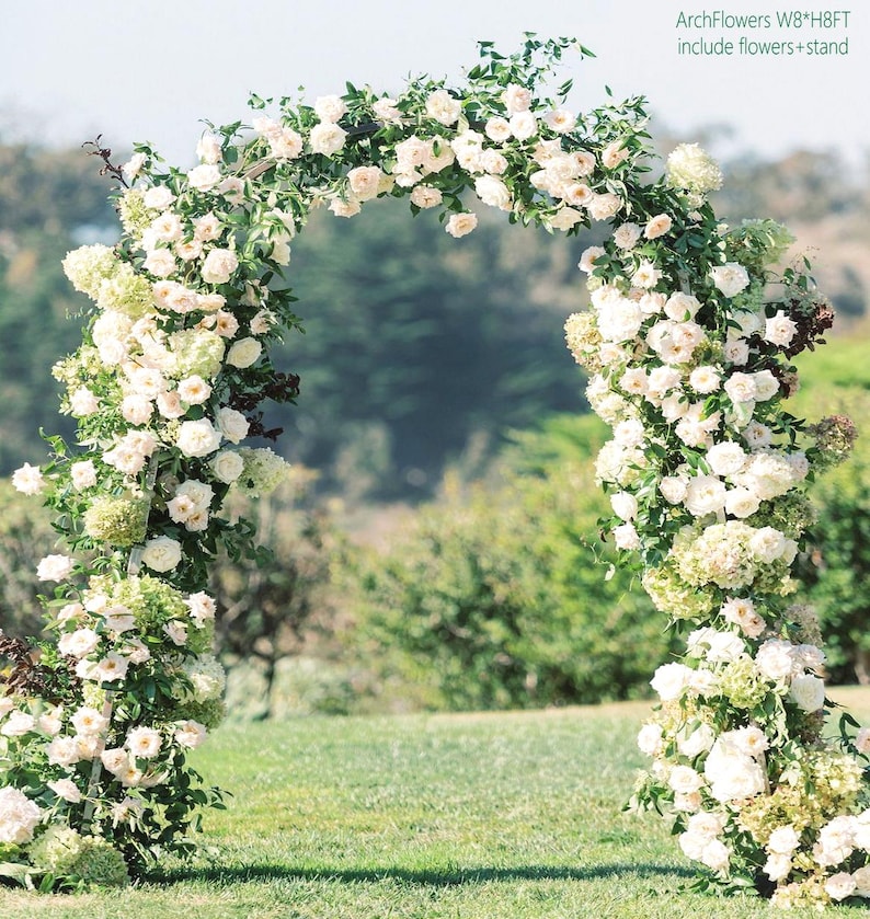 K&ouml;nnte beinhalten: Ein wei&szlig;er Blumenbogen, perfekt f&uuml;r Hochzeiten oder besondere Anl&auml;sse. Der Bogen ist mit &uuml;ppigen wei&szlig;en Rosen und Gr&uuml;n geschm&uuml;ckt und schafft eine romantische und elegante Pr&auml;sentation. Der Text "ArchFlowers W8*H8FT include flowers+stand" ist sichtbar.