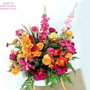May include: A vibrant floral arrangement featuring a variety of colorful flowers in shades of pink, orange, and yellow. The arrangement is approximately 2 feet long, 14-16 inches wide, and 14-22 inches high. The flowers are arranged in a white container.
