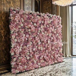 May include: A large, rectangular floral wall made of pink and white roses and other flowers. The flowers are densely packed, creating a textured surface. The wall is set against a dark green backing, suitable for events.