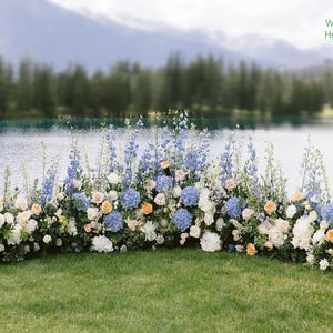 May include: A floral arrangement with blue, white, and peach flowers, set against a backdrop of a lake and mountains. The arrangement is approximately 12 feet long, 14-16 inches wide, and 14-22 inches high. Ideal for weddings or outdoor events.