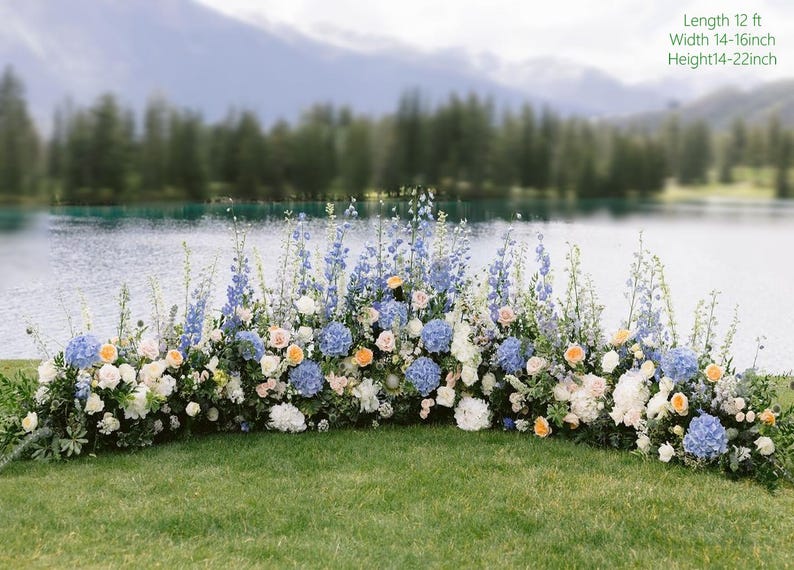 May include: A floral arrangement with blue, white, and peach flowers, set against a backdrop of a lake and mountains. The arrangement is approximately 12 feet long, 14-16 inches wide, and 14-22 inches high. Ideal for weddings or outdoor events.