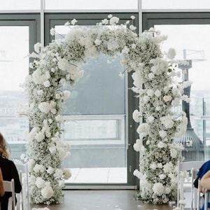 May include: A white floral archway made of baby's breath and white roses, perfect for a wedding ceremony.