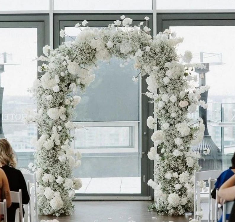 May include: A white floral archway made of baby's breath and white roses, perfect for a wedding ceremony.