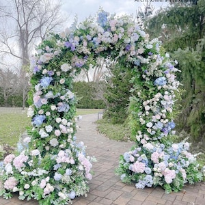 May include: A floral archway, adorned with an abundance of pastel-colored flowers, including white, pink, and blue blooms, creates a picturesque scene. The arch is lush with greenery and the text "ArchFlowers W8xH8 ft" is visible.