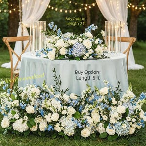 Pode incluir: Uma mesa redonda com uma toalha azul-clara apresenta um centro de mesa floral e um grande arranjo floral na base. O centro de mesa está rotulado como Buy Option: Length 2 ft, e o arranjo da base como Buy Option: Length 5 ft.