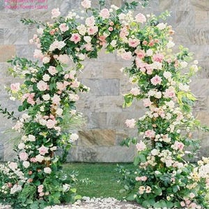 K&ouml;nnte beinhalten: Ein floraler Torbogen mit rosa und wei&szlig;en Rosen und gr&uuml;nem Laub. Der Bogen steht vor einer Steinmauer und gr&uuml;nem Gras. Der Text "ArchFlowers W7*H9FT include flowers + stand" ist sichtbar.