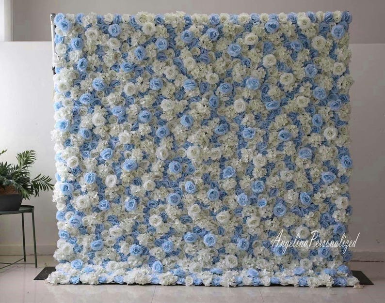 May include: A backdrop made of artificial flowers in white and light blue. The flowers are arranged in a dense pattern, creating a full and lush look. The backdrop is perfect for weddings, parties, or other special events.