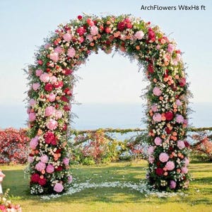 May include: A floral archway, approximately 8 feet wide and 8 feet high, adorned with a variety of pink, red, and white flowers. The arch is set on a grassy lawn with a view of the ocean in the background. Text on the image reads "ArchFlowers W8xH8 ft".