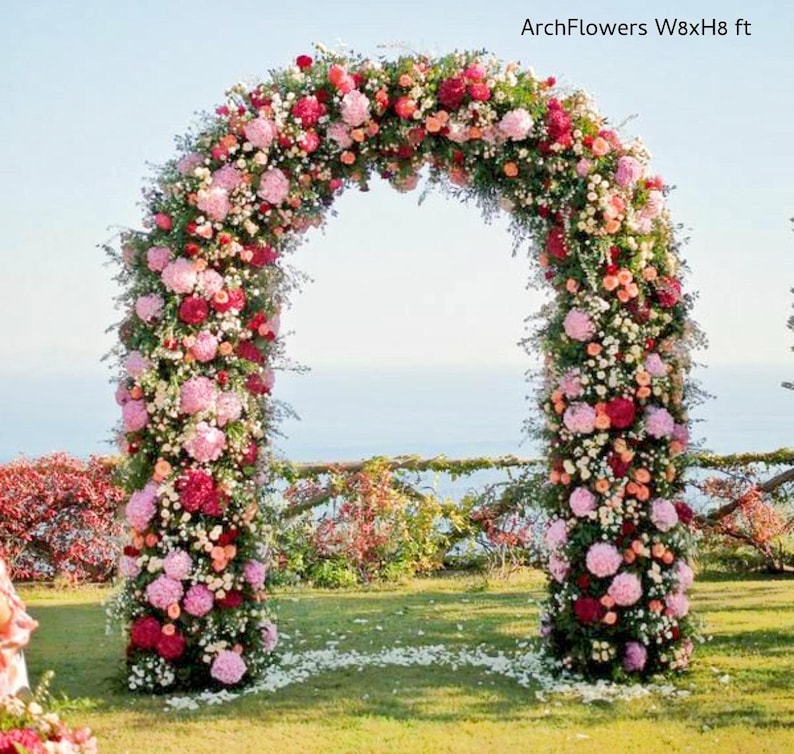 May include: A floral archway, approximately 8 feet wide and 8 feet high, adorned with a variety of pink, red, and white flowers. The arch is set on a grassy lawn with a view of the ocean in the background. Text on the image reads "ArchFlowers W8xH8 ft".