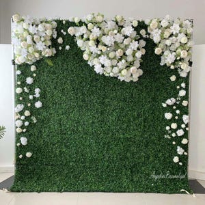 May include: A green artificial grass backdrop with white flowers cascading down the sides. The backdrop is perfect for a wedding, party, or other event. The text "Angelina Personalized" is visible in the bottom right corner.