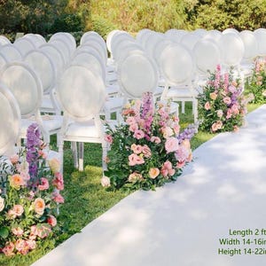 May include: Rows of white oval-back chairs arranged for an event, with floral arrangements of pink and purple flowers placed along a white aisle runner. The floral displays measure 2 feet in length, 14-16 inches in width, and 14-22 inches in height.