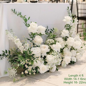 Puede incluir: Arreglo floral blanco con vegetaci&oacute;n, con rosas, hortensias y otras flores blancas. El arreglo mide 1,22 metros de largo, 35-40 cent&iacute;metros de ancho y 40-55 cent&iacute;metros de alto.