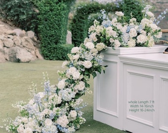 Puede incluir: Una estructura blanca adornada con un arreglo floral de rosas blancas e hortensias azules. El arreglo cae en cascada por el lateral. El texto en la estructura indica una longitud de 2,13 m, un ancho de 35,5-40,6 cm y una altura de 40,6-61 cm.
