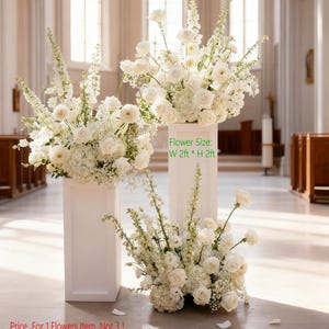 May include: Three white floral arrangements, each with a variety of white flowers, including roses and hydrangeas. The arrangements are displayed on white pedestals. The text on the image says "Flower Size: W 2ft * H 2ft".