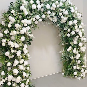 May include: A white floral archway made of white roses and greenery. The archway is perfect for a wedding ceremony or other special event.