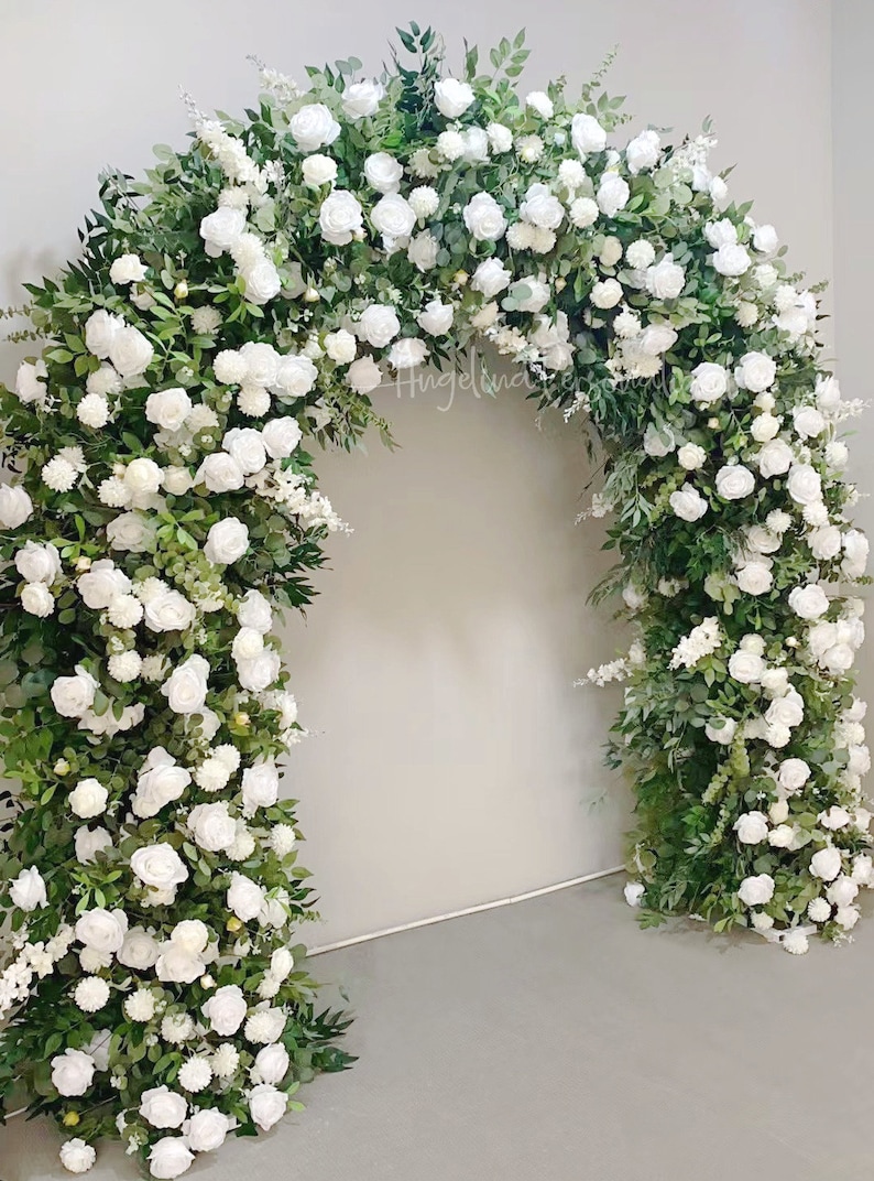 May include: A white floral archway made of white roses and greenery. The archway is perfect for a wedding ceremony or other special event.